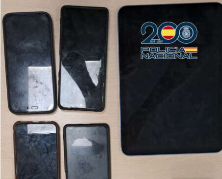 Evidence laid out on a table: six smartphones, a smartwatch, charging cables, and a Policía Nacional notebook/logoed pad.