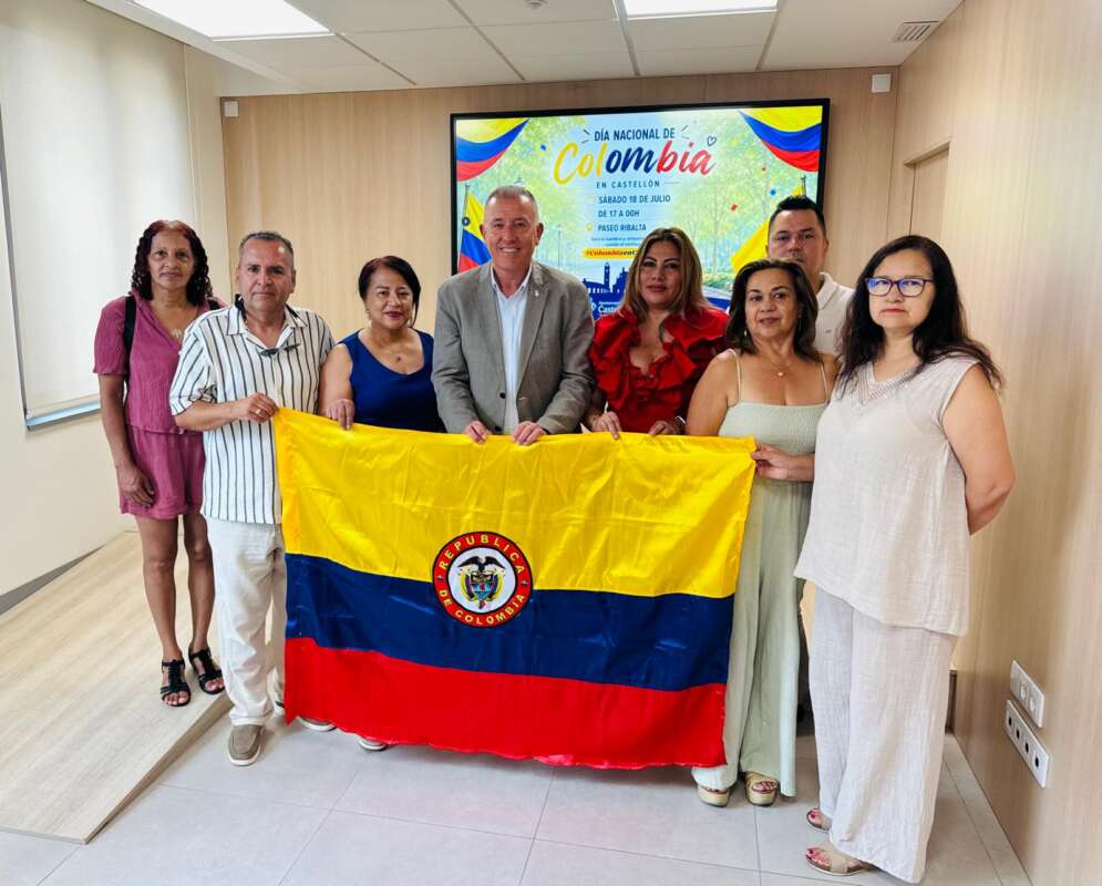 Eight people in an office holding a Colombian flag, posing for a group photo during a National Day celebration.