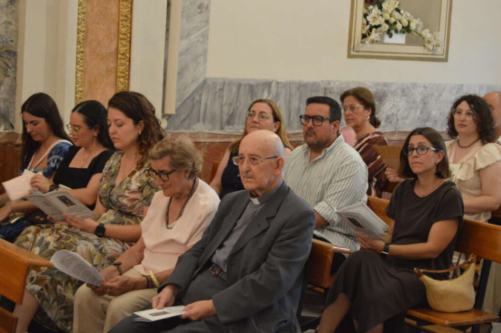 Group of adults seated in church pews, reading programs during a ceremony in a marble-lined interior