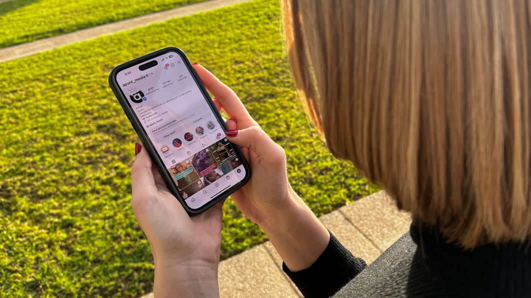 Person outdoors, holding a smartphone and scrolling through a social media feed on the screen.