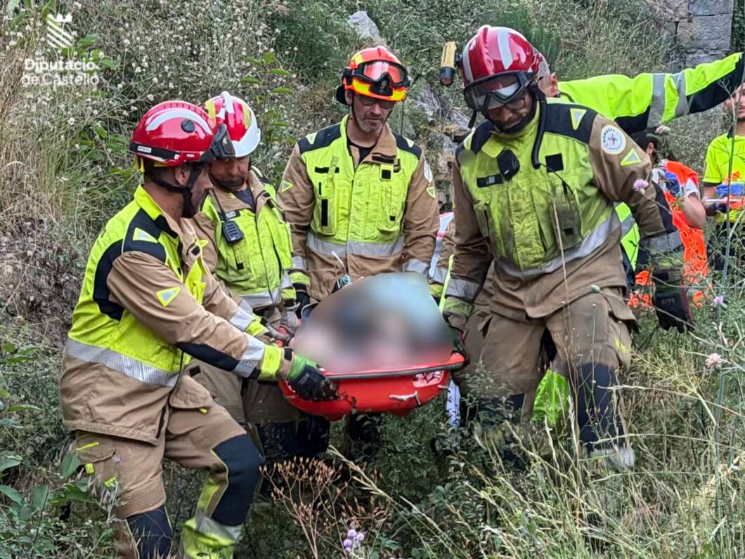 Rescue team in neon uniforms and helmets carefully carries a red stretcher through tall grass with a blurred patient on the stretch.
