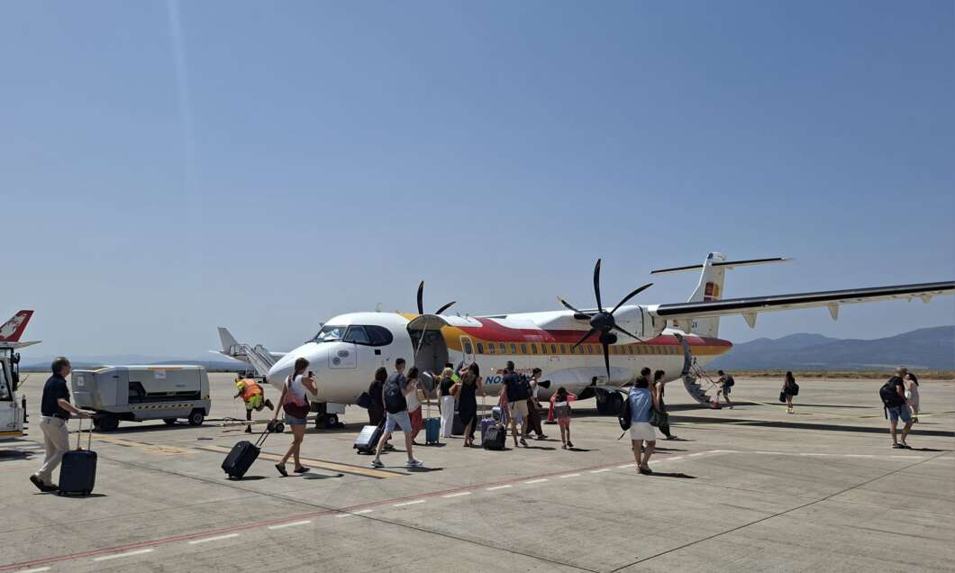 Passengers with luggage boarding a small propeller airplane on a sunny airport tarmac.