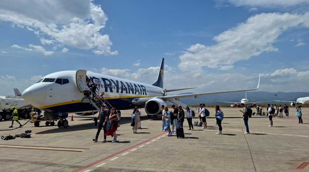 Passengers boarding a Ryanair airplane via mobile stairs on a sunny tarmac.
