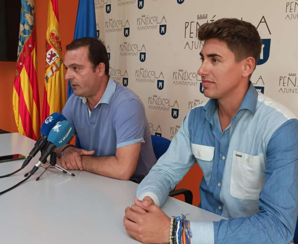Two men sit at a press conference table with microphones in front; backdrop displays PEÑÍSCOLA AJUNTAMENT logo and flags behind them.