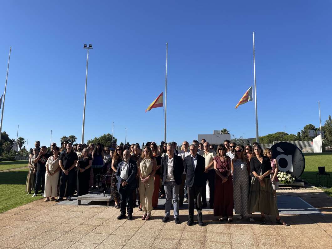 Group of formally dressed people posing for a photo at an outdoor ceremony, clear blue sky and flagpoles in the background.
