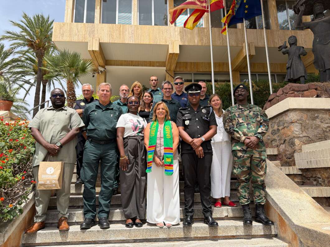 Group of diverse officials and civilians posing on steps in front of a beige government building with flags.