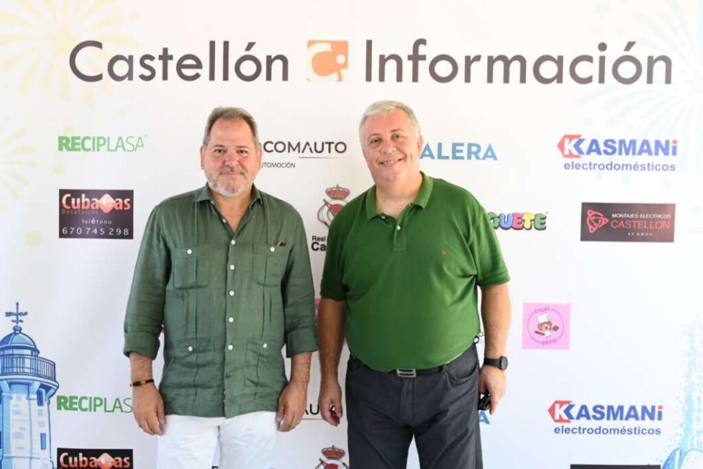 Two men pose in front of a Castellón Información backdrop with sponsor logos, both wearing green shirts and smiling at the camera.