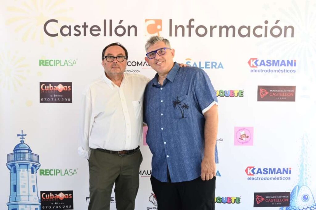 Two men posing together in front of a Castellón Información backdrop with sponsor logos on the wall.