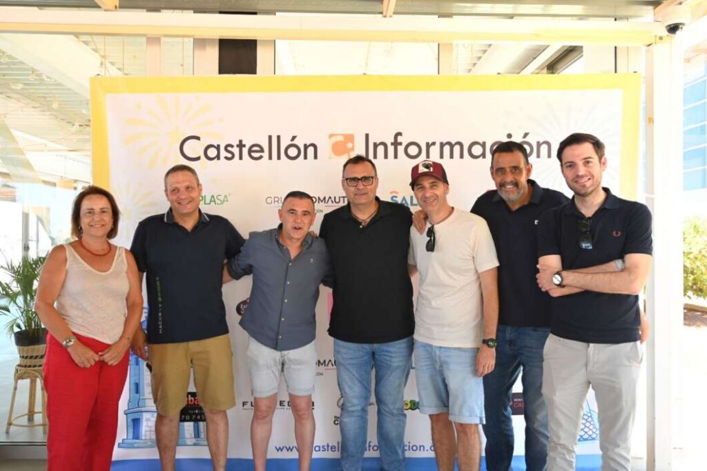 Group of seven adults posing together in front of a Castellón Información banner at an event.