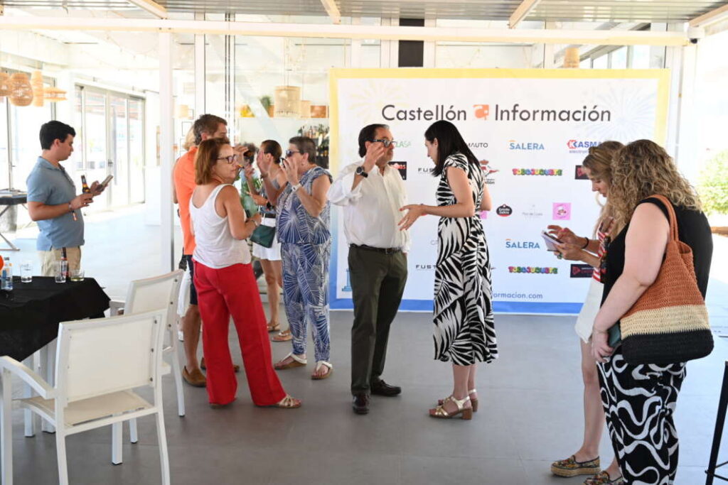 Informal networking event with people chatting in front of a Castellón Información banner inside a bright venue.