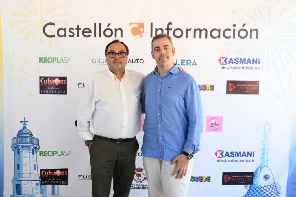 Two men pose together in front of a 'Castellón Información' backdrop at a formal event. Left: older man in white shirt and dark trousers; right: younger man in blue shirt and light pants, both smiling. Backdrop features sponsor logos and a lighthouse illustration.