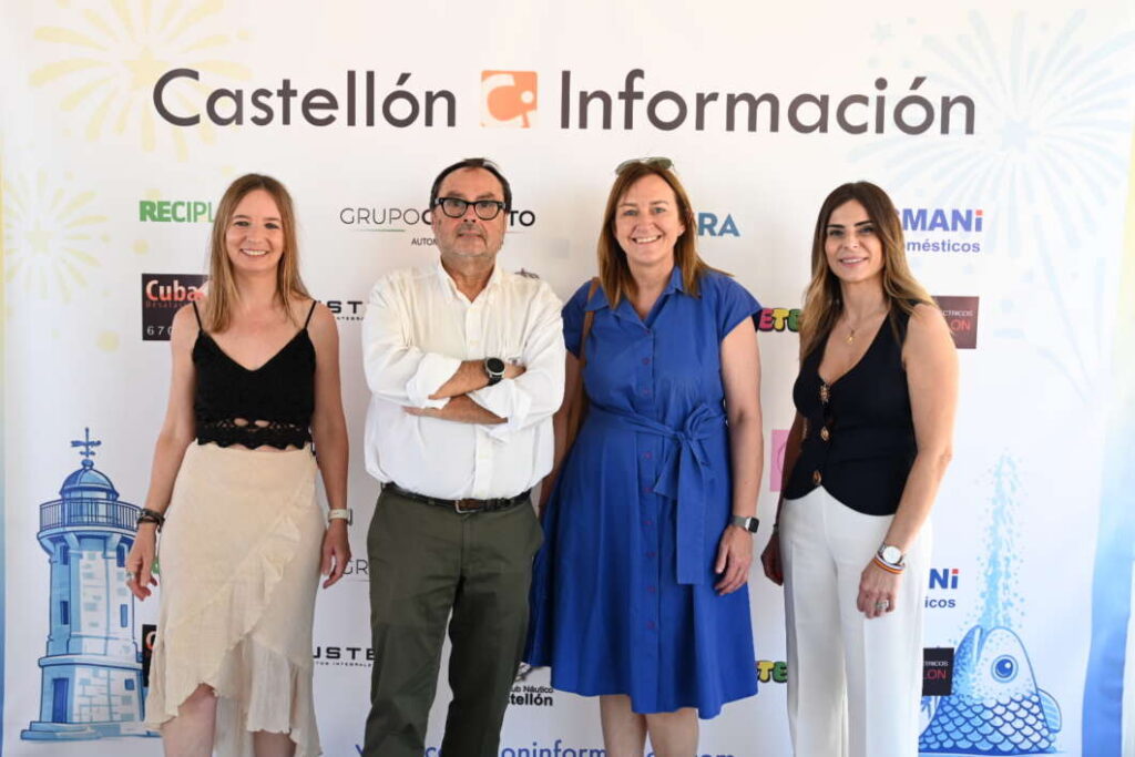 Four adults posing for a photo in front of a Castellón Información backdrop, two women in dresses and a man and a woman in smart casual attire, all smiling in a row.]','Four people stand side by side in front of a Castellón Información banner with sponsor logos, smiling at the camera.