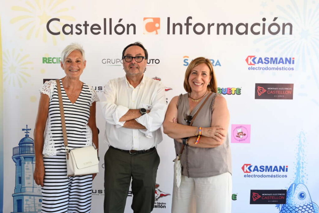 Three adults pose in front of a Castellón Información backdrop: a striped-dress woman with a white bag, a man in a white shirt with glasses, and a sleeveless beige-top woman.