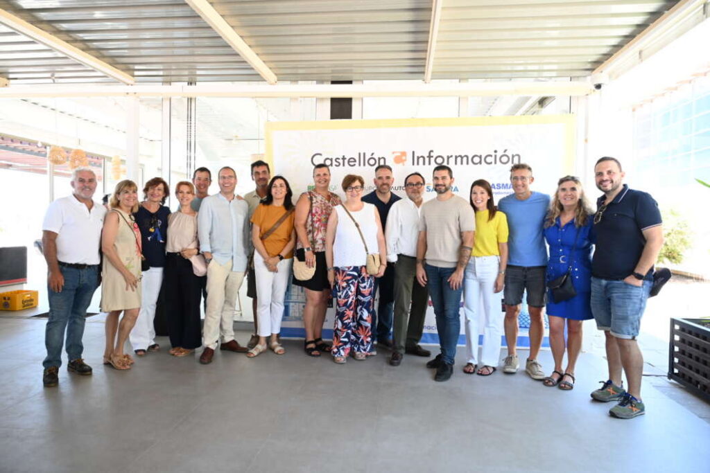 Group of about 18 adults posing together in front of a banner reading 'Castellón Información' under a covered outdoor area at an event.