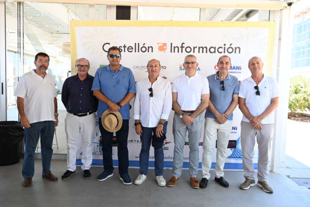 Eight men in smart casual attire pose for a group photo in front of a Castellón Información banner at an event.