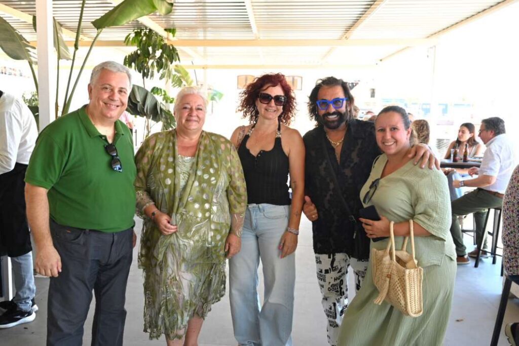 Group of five adults smiling for a photo at an outdoor/covered venue, dressed casually in summer clothes.