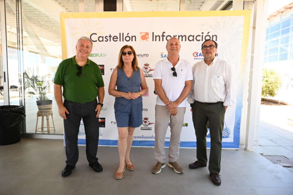 Four adults stand in a row for a photo in front of a Castellón Información banner at an event, indoors with natural light.