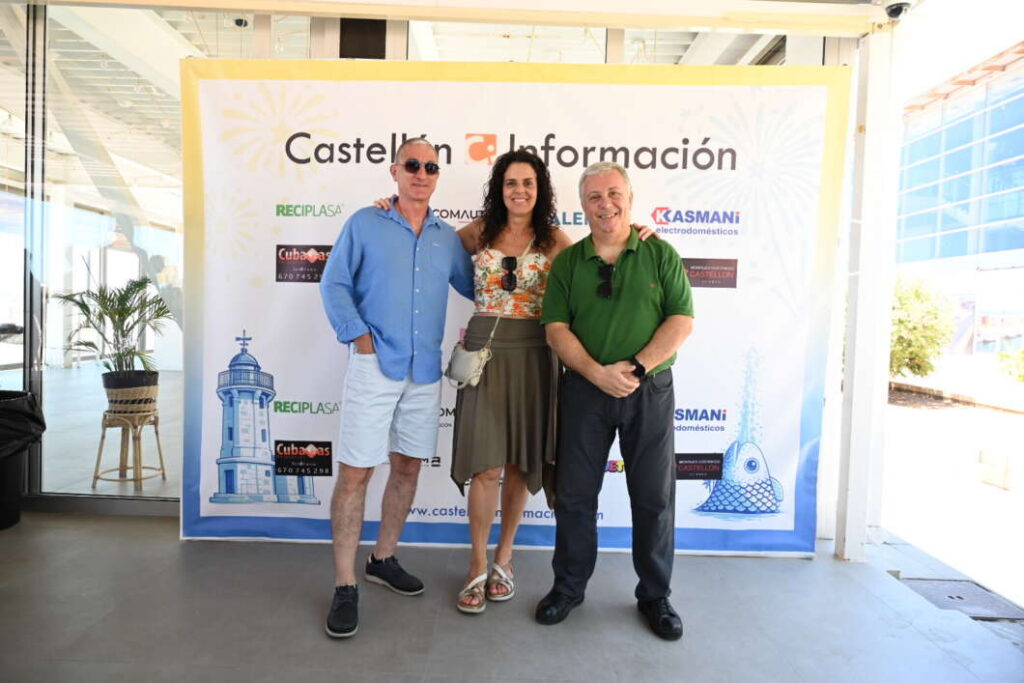 Three adults pose together in front of a Castellón Información banner in a bright indoor space, smiling for the photo.