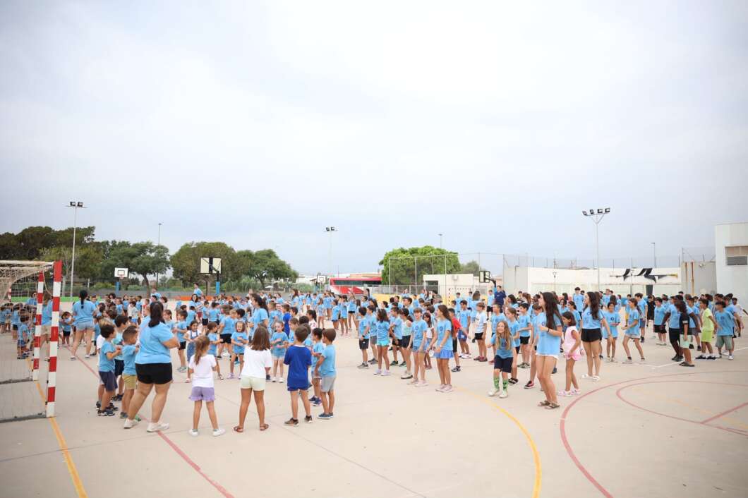 Large group of children in blue shirts standing in circles on a school outdoor basketball court for a group activity. **(informative)**