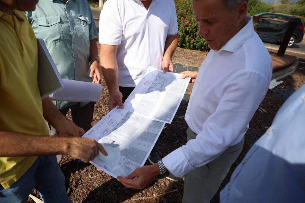 Group of men in casual shirts examining large blueprint plans outdoors at a construction site.