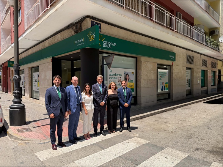 Six businesspeople in formal attire posing on a street crosswalk outside a Eurocaja Rural bank.