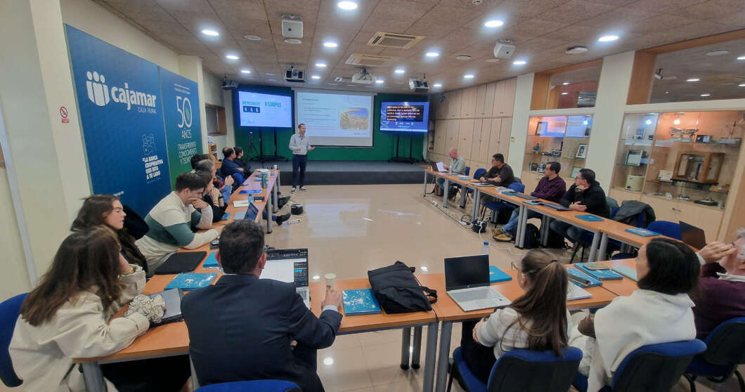 Workshop session in a modern conference room with participants seated around a U-shaped table facing a presenter and two screens at the front.