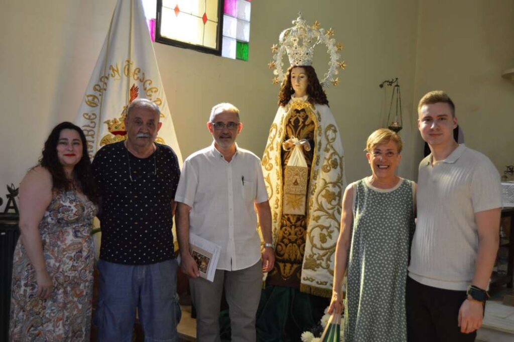 Six people stand together in a church, posing in front of an ornate statue of Mary in ceremonial robes and halo.