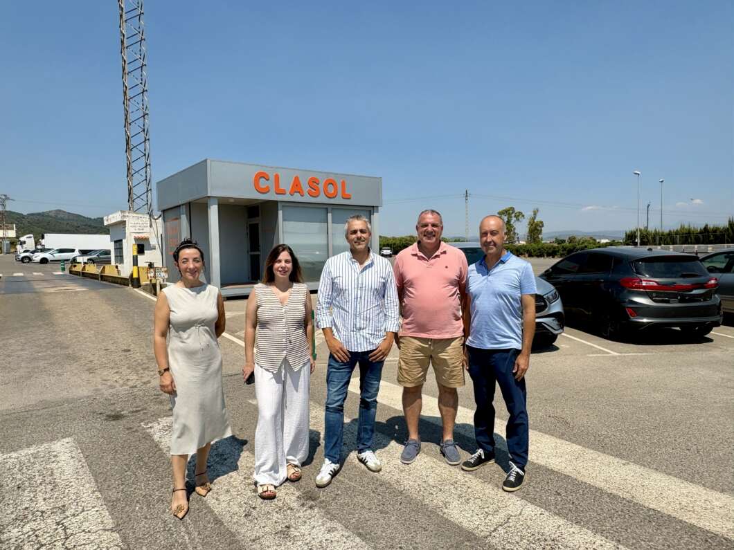 Five people stand together in a parking lot in front of a gray building labeled CLASOL on a sunny day.