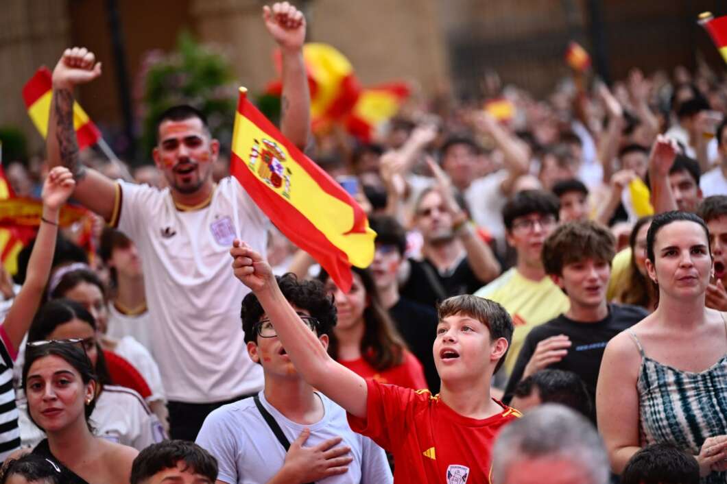Crowd of cheering sports fans waving Spanish flags at a celebration.