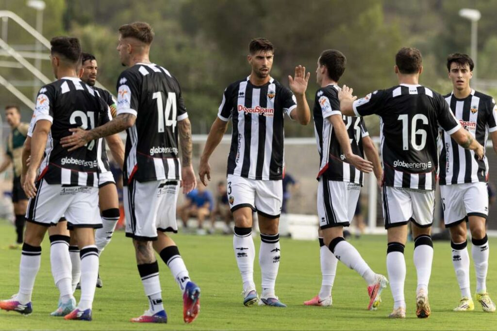 Soccer players in black-and-white striped uniforms on a green field high-fiving each other after a play.