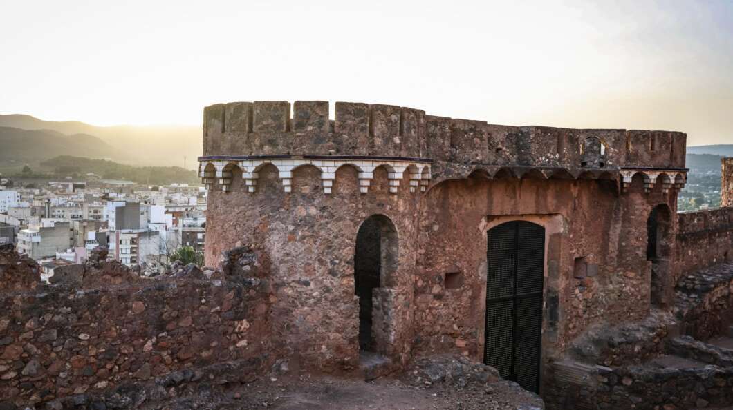 Ancient stone fortress wall with crenellations overlooking a town at sunset.