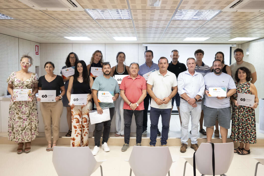 Group of 15 adults posing with certificates on a stage during an awards ceremony in a bright room.