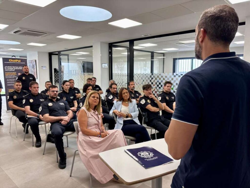 Instructor speaks to a seated group of uniformed officers in a classroom; two women in front row listen attentively.