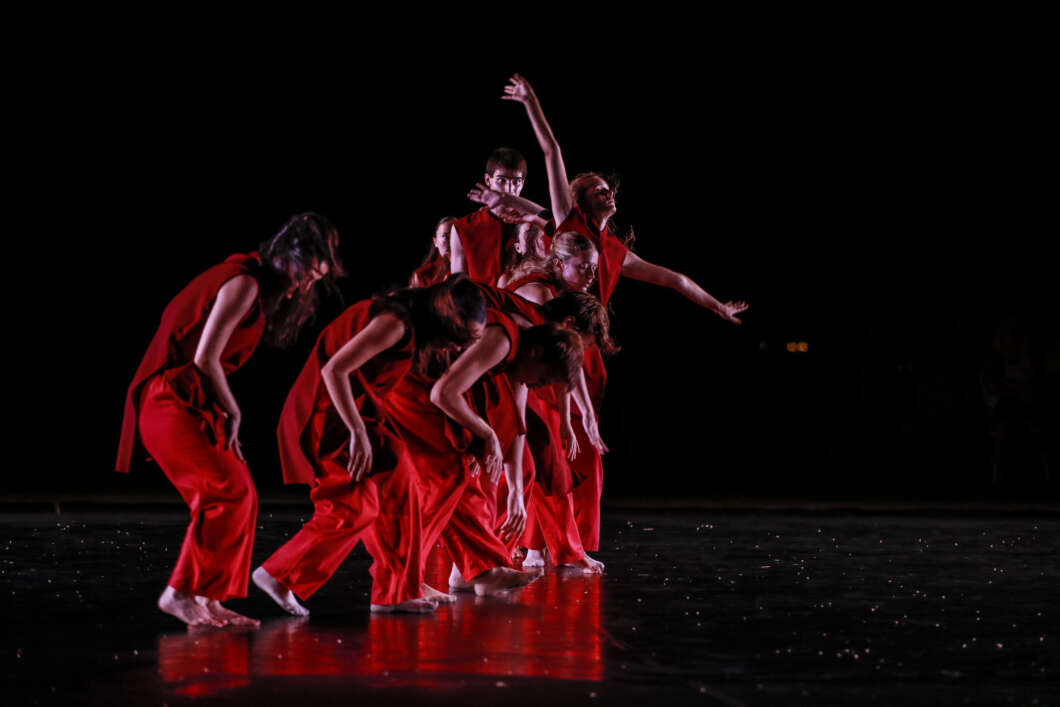 Group of dancers in red outfits performing a contemporary routine on a dark stage.