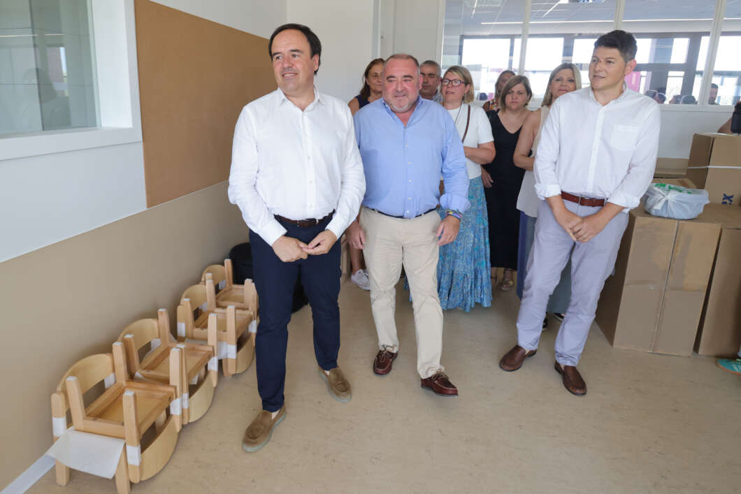 Group of professionals touring a room with stacked wooden chairs and large boxes on the right.