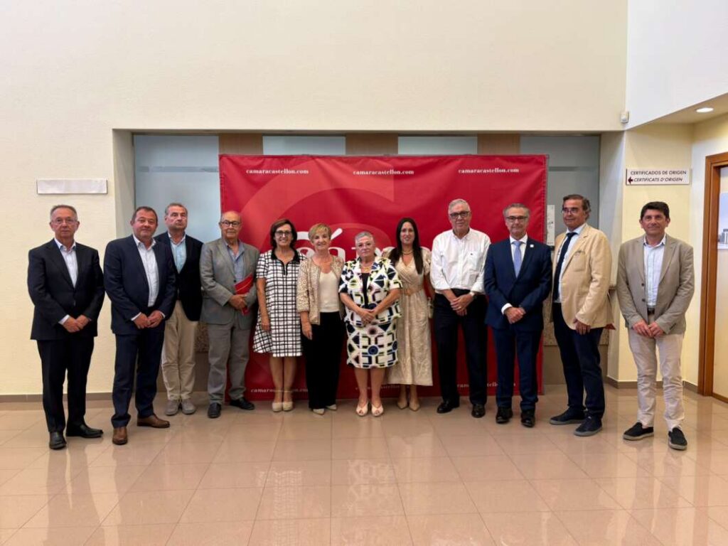 Group of professionals in suits and dresses posing for a photo indoors in front of a red event banner.