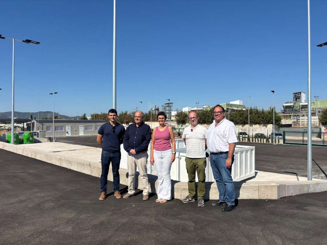 Five people stand together on a paved area beside a construction site under a clear blue sky, posing for a photo.