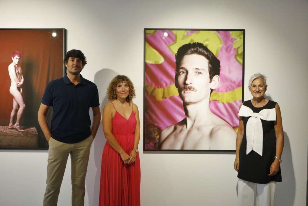 Three visitors stand in an art gallery beside large colorful portraits on a white wall, posing for the photo.