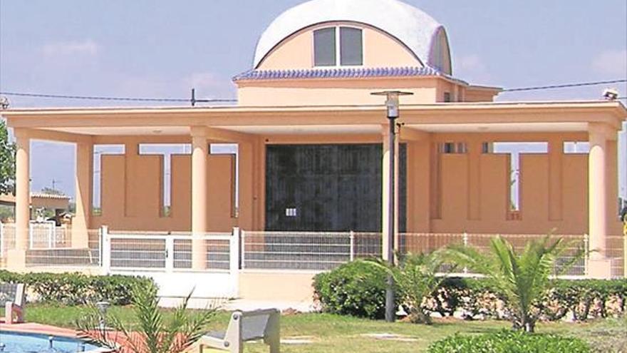 Peach-colored villa-style building with a rounded dome roof, tall columns, and a white fence in a landscaped yard.