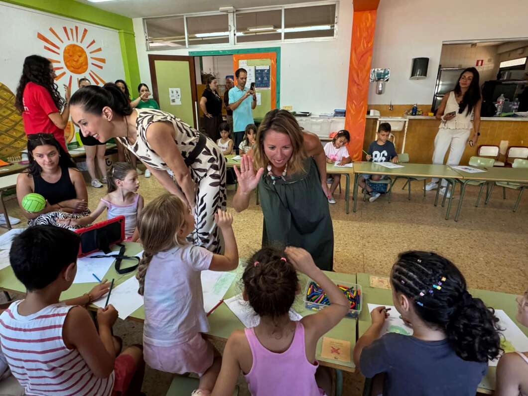 Teachers high-five seated children at a colorful classroom table during an art activity.