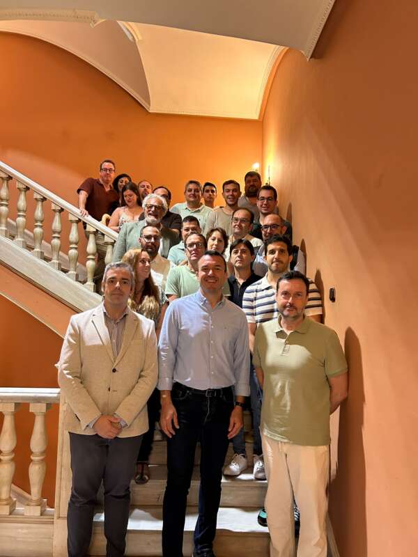 Group of adults posing on a curved staircase against orange walls in a warmly lit interior (team photo).
