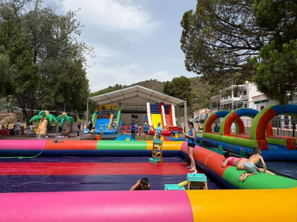 Colorful inflatable water park with slides and children playing under a white canopy in a sunny outdoor area.