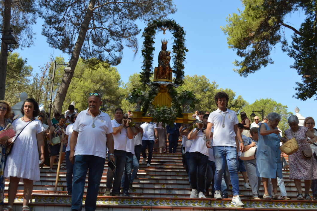 Group of people in white shirts carrying a decorated statue on a floral arch down a tiled staircase during an outdoor procession.