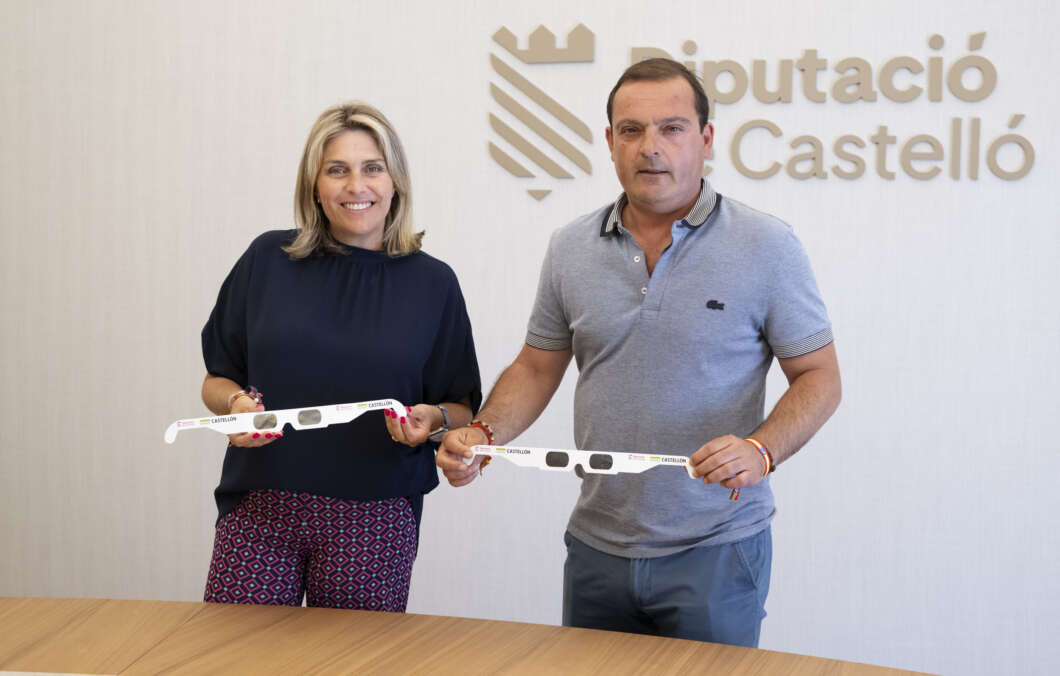 Man and woman stand in front of a Diputació Castelló sign, smiling, each holding a white strip with cut-out sunglasses.