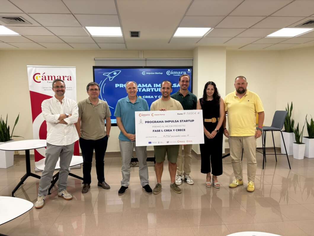 Group of seven people posing in a bright room, holding a large check for the Impulsa Startup program.