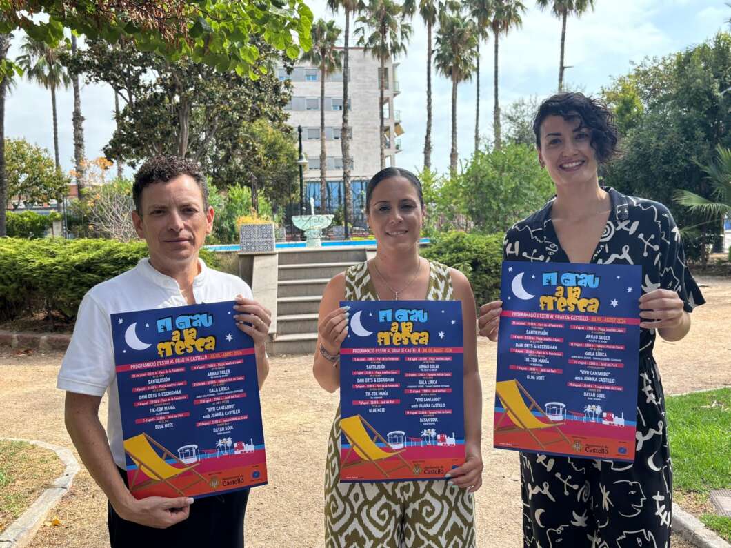 Three adults stand in a park holding blue event posters with a crescent moon and stars, smiling at the camera.