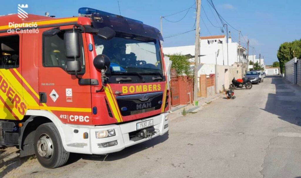 Red fire truck labeled BOMBERS parked on a sunny residential street with houses and wires in the background (Spain, Diputació de Castelló logo visible).