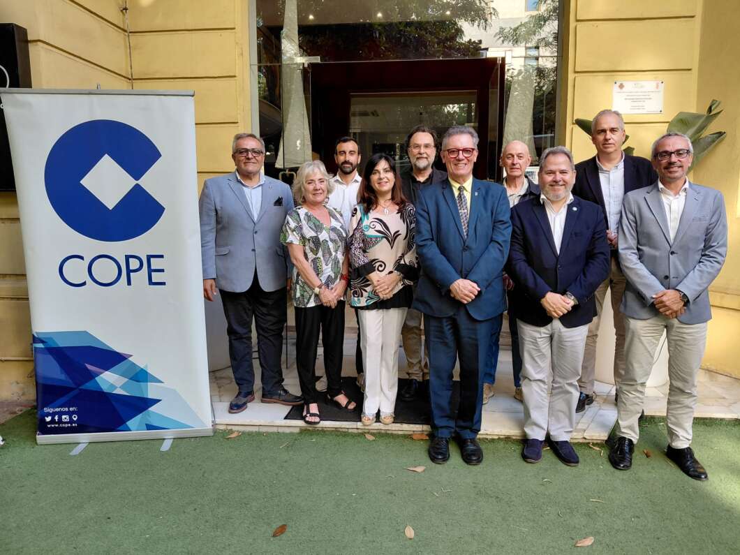 Eleven adults in business attire pose on a doorway step beside a COPE banner outdoors.