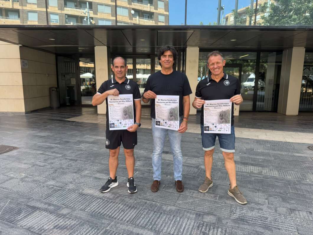 Three men stand outside a modern building, each holding a printed poster or flyer facing the camera.