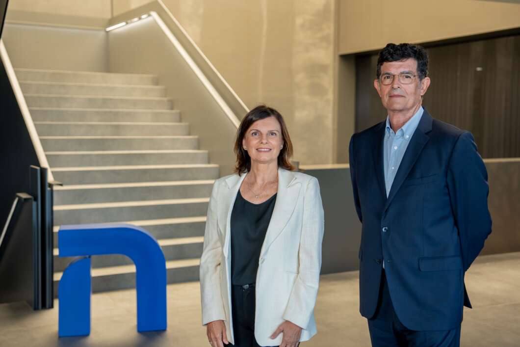 Two professionals stand in a modern lobby; a woman in a light blazer and a man in a navy suit.